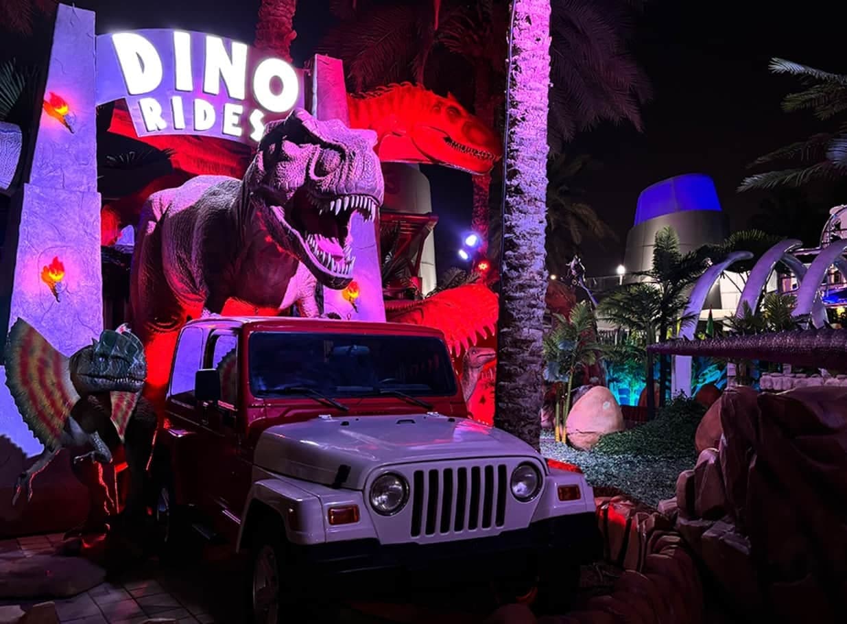 A life-size T. rex and a jeep lit red at night in Dinosaur Park at Dubai Garden Glow