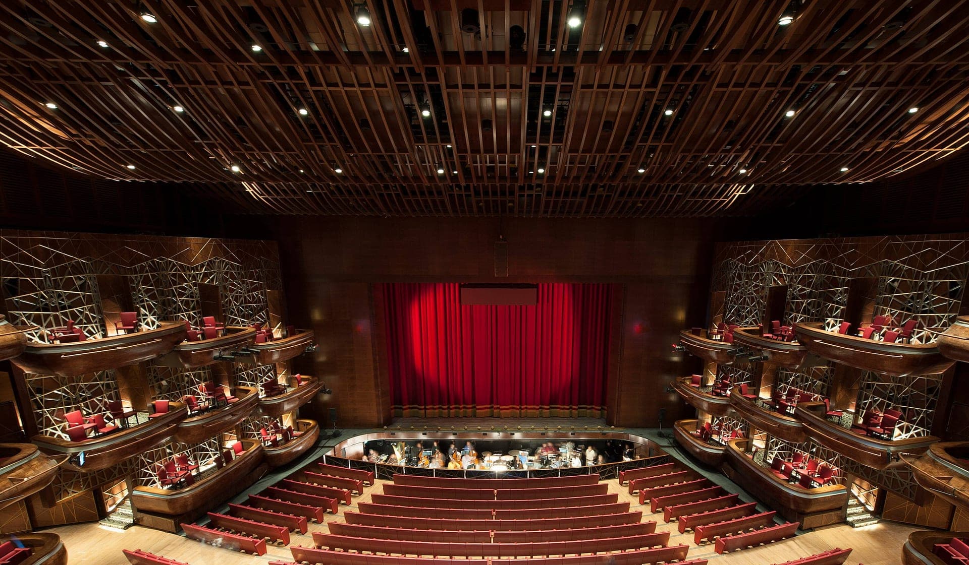 Inside Dubai Opera, with the red curtain, tiered seating and sculpted ceiling
